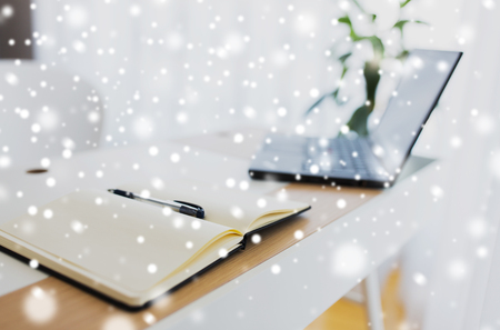 business, objects and education concept - notebook or diary with pen and laptop computer on office table over snowの写真素材