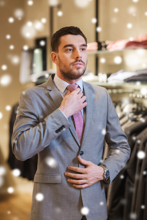 sale, shopping, fashion, business style and people concept - elegant young man choosing and trying on suit and tie in mall or clothing store over snowの写真素材