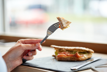 food, dinner and people concept - woman eating salmon panini sandwich with tomatoes and cheese at restaurantの写真素材