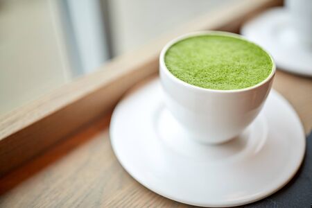 drink, diet, weight-loss and slimming concept - white cup of matcha green tea latte on table at...