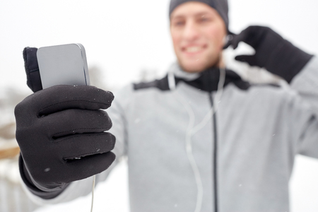 fitness, sport, people, technology and healthy lifestyle concept - close up of happy smiling young man in earphones with smartphone listening to music in winterの写真素材