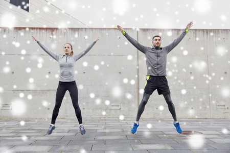 fitness, sport, people, exercising and healthy lifestyle concept - happy man and woman jumping outdoors over snowの写真素材