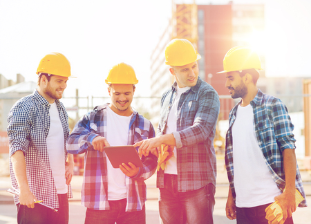 business, building, teamwork, technology and people concept - group of smiling builders in hardhats with tablet pc computer and clipboard outdoorsの写真素材