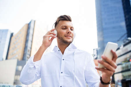 people, technology and lifestyle - happy young man with headphones and smartphone listening to music in cityの写真素材