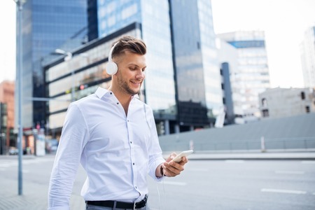 people,  technology and lifestyle - happy young man with headphones and smartphone listening to music in cityの写真素材