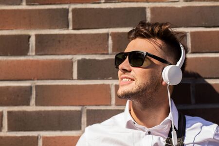 music, technology and people concept - happy smiling young man in headphones and sunglasses over...