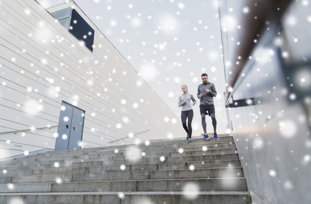 fitness, sport, people, exercising and healthy lifestyle concept - couple of sportsmen running downstairs outdoors over snowの写真素材