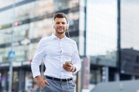 people, technology and lifestyle - happy young man with headphones and smartphone listening to music in cityの写真素材