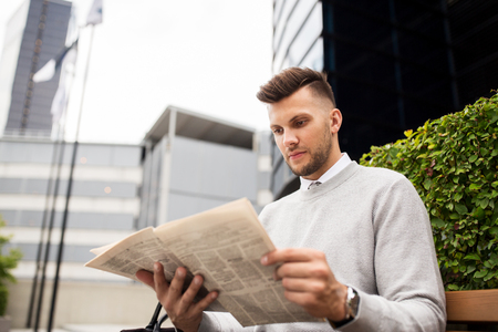 business, mass media and people concept - man reading newspaper on city street benchの写真素材