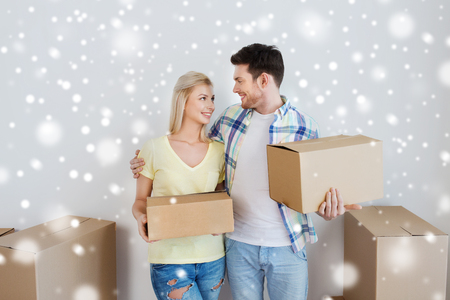 home, people, repair and real estate concept - smiling couple with big cardboard boxes moving to new place over snowの写真素材