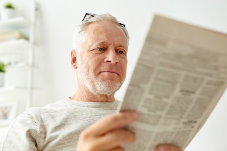 information, people, and mass media concept - close up of senior man reading newspaper at homeの写真素材