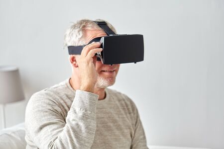 technology, augmented reality, gaming, entertainment and people concept - senior man with virtual headset or 3d glasses playing videogame at homeの写真素材