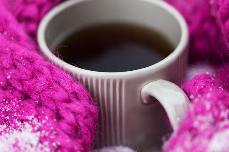 season, drinks, christmas and winter holidays concept - close up of tea or coffee mug and knitted woolen scarf in snowの写真素材