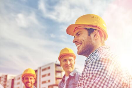 business, building, teamwork and people concept - group of smiling builders in hardhats at construction siteの写真素材