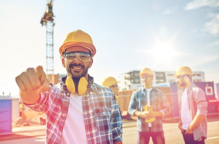 business, building, teamwork and people concept - group of smiling builders in hardhats pointing finger at you on construction siteの写真素材
