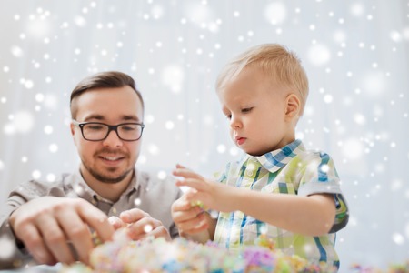 family, childhood, creativity, activity and people concept - happy father and little son playing with ball clay at home over snowの写真素材