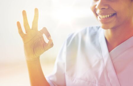 gesture, people and medicine concept - close up of happy african female doctor or nurse showing ok sign at hospitalの写真素材