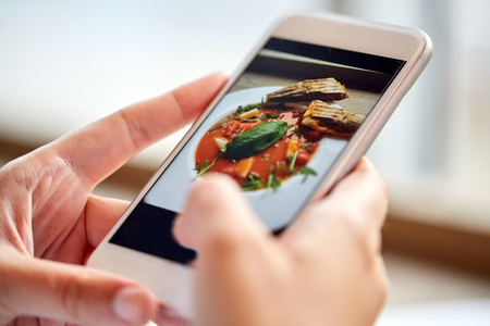 food, eating, technology, culinary and people concept - woman hands with gazpacho soup photo on smartphone screen at restaurantの写真素材