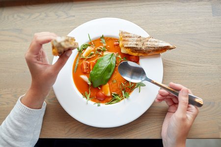 food, dinner, culinary and people concept - woman eating gazpacho soup with sandwich and spoon at restaurantの写真素材