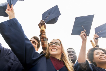 education, graduation and people concept - group of happy international students in bachelor gowns waving mortar boards or hatsの写真素材