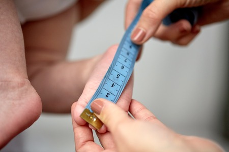 close up of hands with tape measuring baby footの写真素材