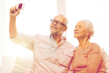 family, technology, age and people concept - happy senior couple taking selfie with camera at homeの写真素材