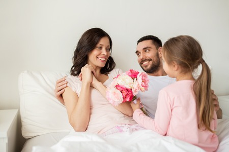 happy girl giving flowers to mother in bed at homeの写真素材