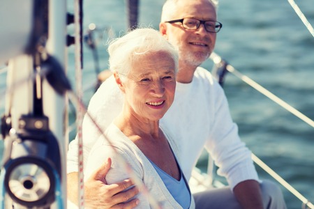 sailing, age, tourism, travel and people concept - happy senior couple hugging on sail boat or yacht deck floating in seaの写真素材