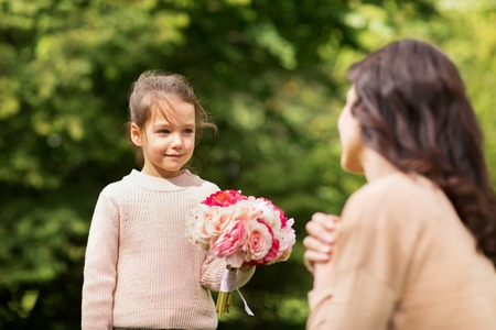 girl giving with flowers to mother in summer parkの写真素材