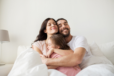 happy family hugging in bed at homeの写真素材