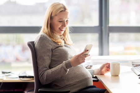 pregnant businesswoman with smartphone at officeの写真素材