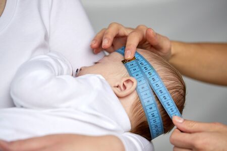 close up of hands with tape measuring baby headの写真素材