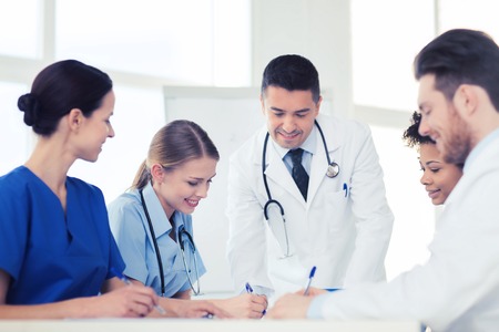 hospital, profession, people and medicine concept - group of happy doctors meeting and taking notes at medical officeの写真素材