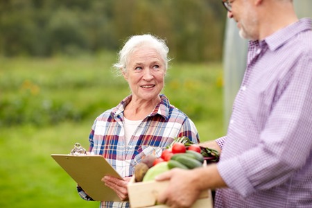farming, gardening, agriculture, harvesting and people concept - senior couple with box of vegetables and clipboard at farmの写真素材