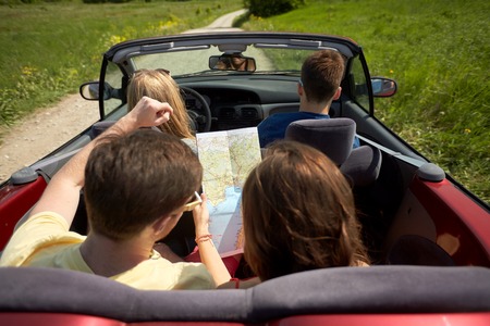 happy friends with map driving in convertible carの写真素材