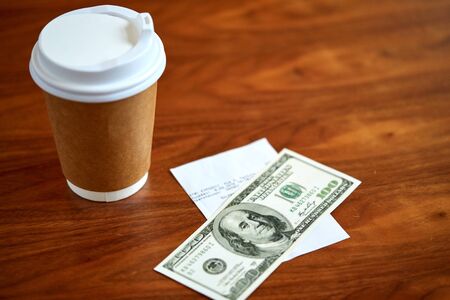 coffee in paper cup, bill and money on tableの写真素材