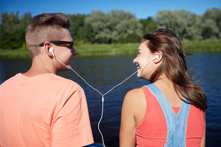 happy teenage couple with earphones on river berthの写真素材
