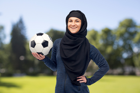sport, fitness, soccer and people concept - happy muslim woman in hijab with football over summer natural backgroundの写真素材