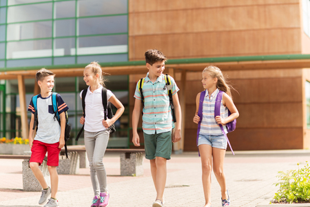 primary education, friendship, childhood, communication and people concept - group of happy elementary school students with backpacks walking and talking outdoorsの写真素材