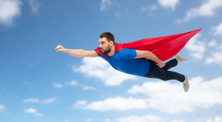 man in red superhero cape flying over blue skyの写真素材