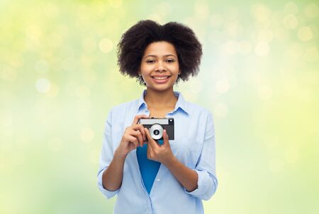 people and photography portrait concept - happy african american young woman with film camera over...