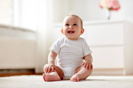 childhood, babyhood and people concept - happy little baby boy or girl sitting on floor at homeの写真素材