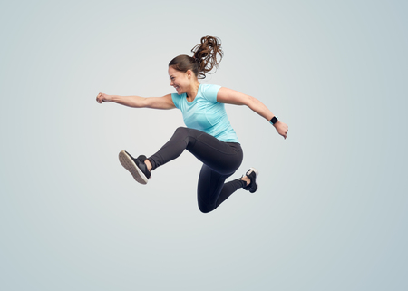 sport, fitness, motion and people concept - happy smiling young woman jumping in air over blue background