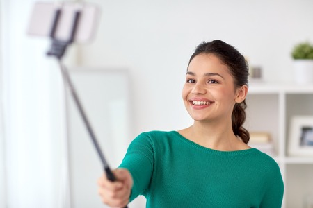 woman taking selfie by smartphone monopod at homeの写真素材