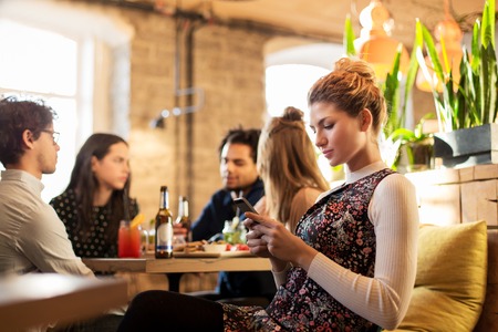 woman with smartphone and friends at restaurant