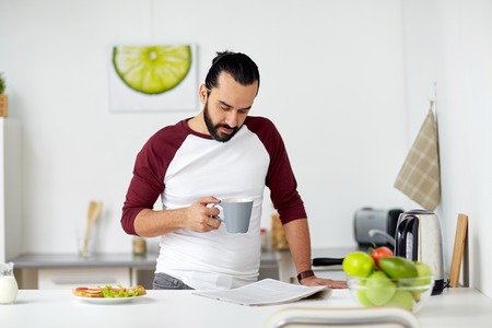 man reading newspaper and eating at home kitchenの写真素材