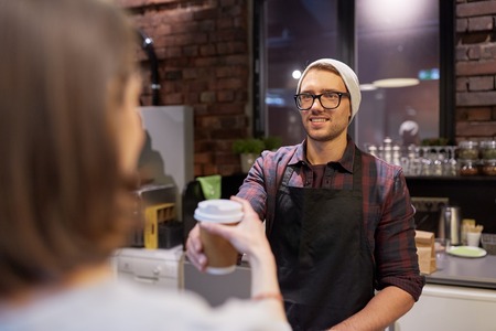 seller giving coffee cup to woman customer at cafeの写真素材