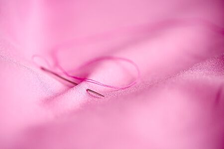 sewing needle with thread stuck into pink fabricの写真素材