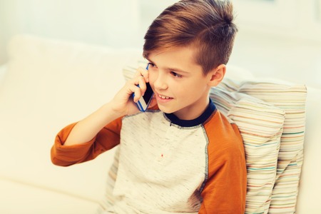 leisure, children, technology, communication and people concept - smiling boy calling on smartphone at homeの写真素材