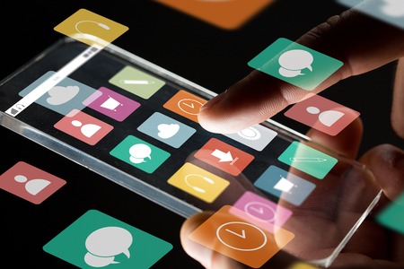 business, multimedia, people and modern technology concept - close up of businessman hand with transparent smartphone with menu icons on screen over black backgroundの写真素材